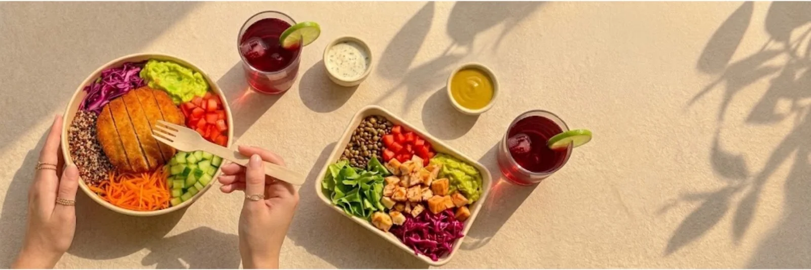 Dos bowls Bonabowl sobre una mesa clara: uno con milanesa, quinua y col morada, otro con pollo, lentejas y guacamole, acompañados de refrescos y salsas